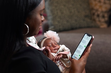 Karimah Ferguson holds her baby while looking at text messages on her cell phone that she sent to Penn Medicine when monitoring her blood pressure after her delivery.